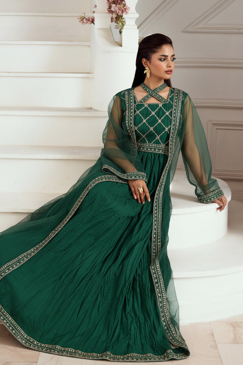 A woman models an olive green traditional Indian gown with gold embroidery and sheer beige sleeves, posing on white stone stairs.